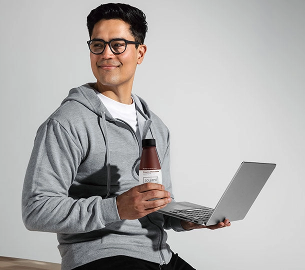 A man at a desk with a laptop and a chocolate Soylent